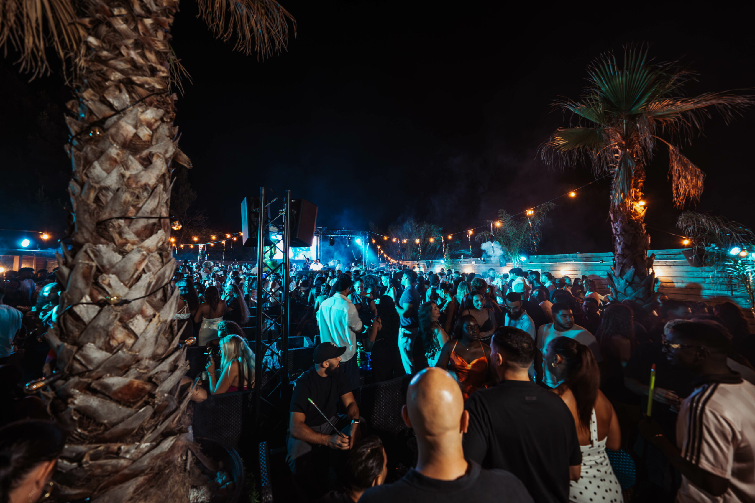 Soirée estivale animée sous les palmiers au club le-five à montpellier, foule dansant sous lumières bleues
